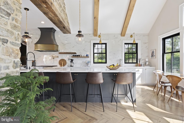 kitchen with custom range hood, light parquet floors, backsplash, beamed ceiling, and hanging light fixtures