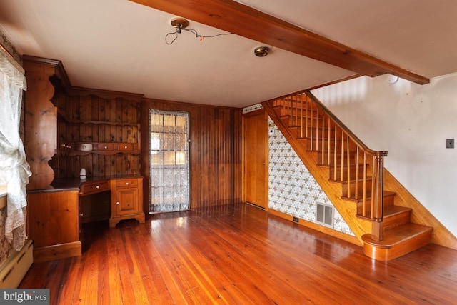 unfurnished living room with wooden walls, baseboard heating, beam ceiling, and hardwood / wood-style floors