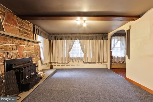 unfurnished living room with dark colored carpet, a healthy amount of sunlight, and beam ceiling