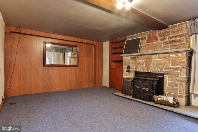 unfurnished living room with a fireplace, carpet, wooden walls, and a wood stove