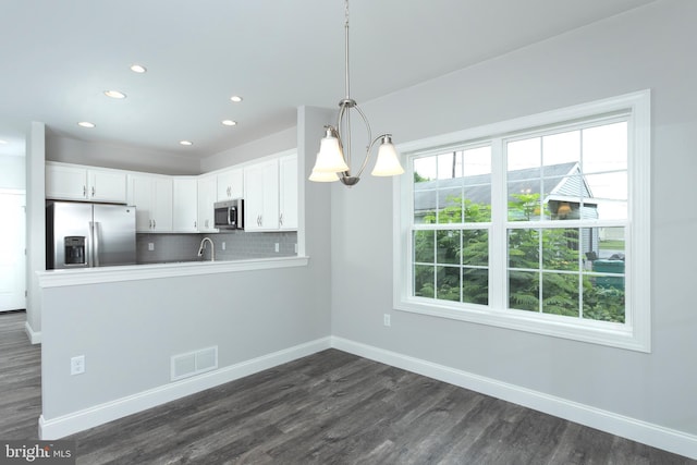 kitchen with kitchen peninsula, white cabinets, pendant lighting, stainless steel appliances, and backsplash