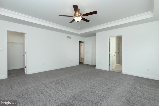 unfurnished bedroom featuring a raised ceiling, ornamental molding, carpet floors, and a spacious closet