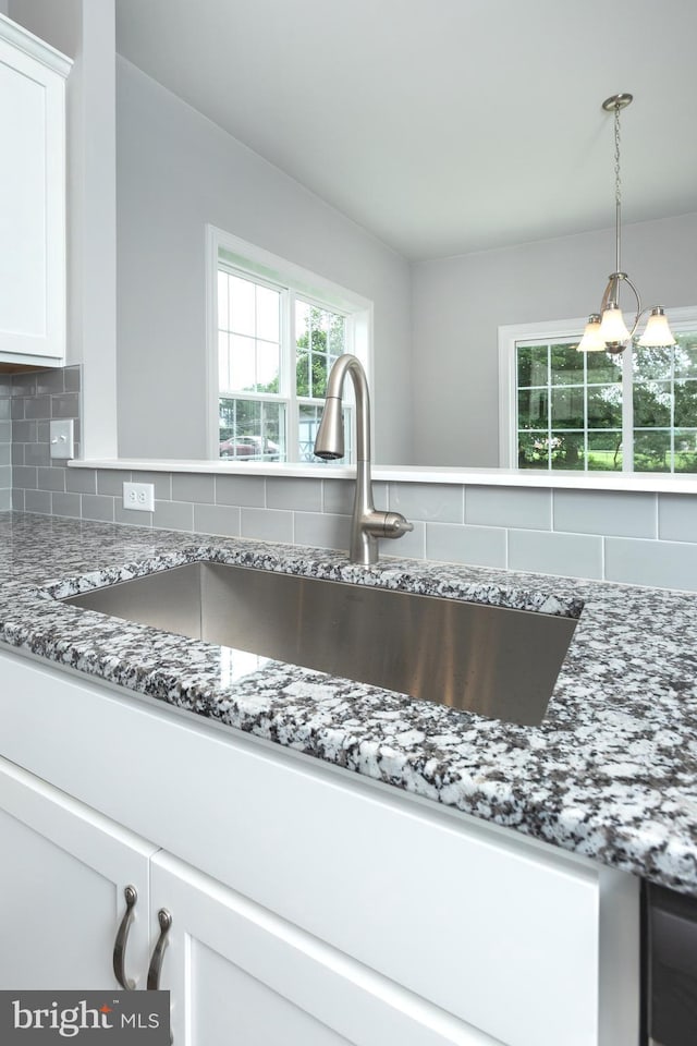 details featuring stone counters, decorative light fixtures, white cabinetry, sink, and backsplash