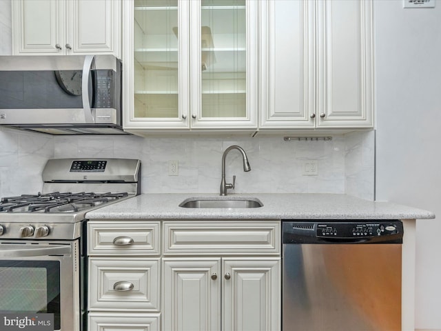 kitchen with appliances with stainless steel finishes, backsplash, a sink, and white cabinets