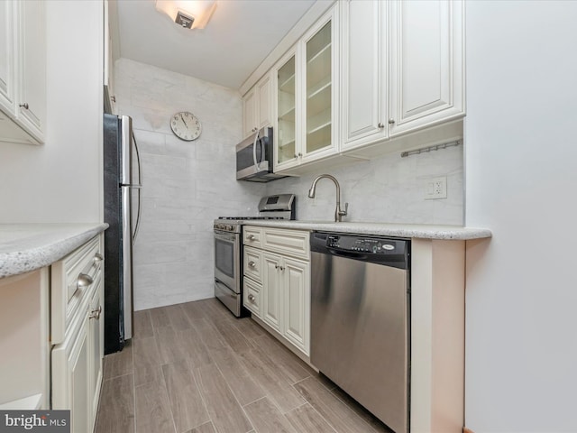 kitchen featuring glass insert cabinets, appliances with stainless steel finishes, a sink, wood finish floors, and backsplash