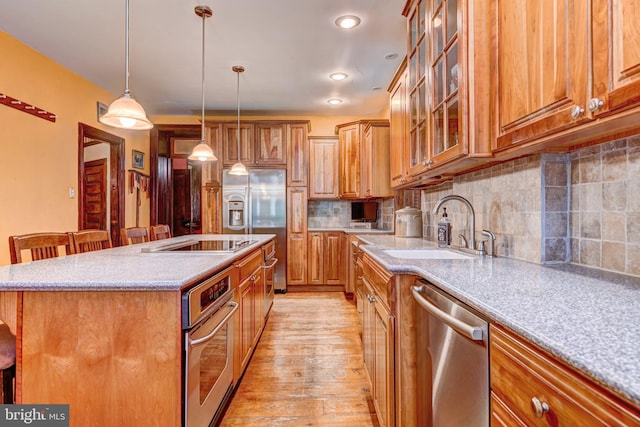 kitchen featuring tasteful backsplash, stainless steel appliances, a kitchen island with sink, light stone countertops, and light hardwood / wood-style flooring