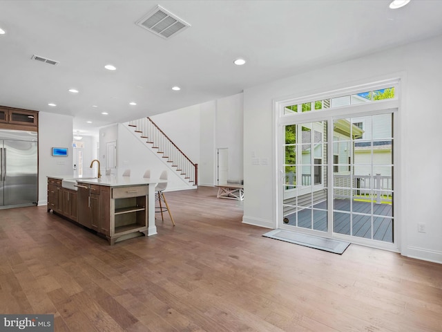 kitchen with stainless steel built in refrigerator, sink, a kitchen island with sink, and hardwood / wood-style floors