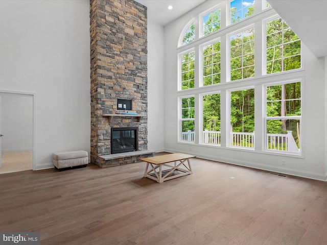 unfurnished living room with hardwood / wood-style flooring, a towering ceiling, a healthy amount of sunlight, and a fireplace