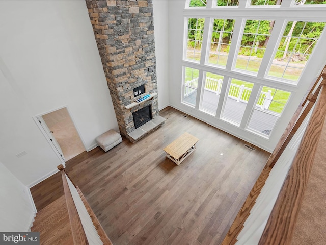 unfurnished living room featuring hardwood / wood-style flooring, a stone fireplace, and a high ceiling