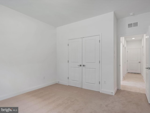 unfurnished bedroom with light colored carpet and a closet