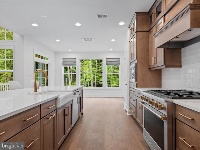 kitchen with appliances with stainless steel finishes, tasteful backsplash, sink, custom exhaust hood, and light hardwood / wood-style floors