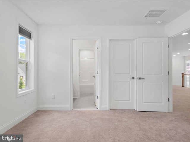 unfurnished bedroom featuring light carpet and ensuite bathroom