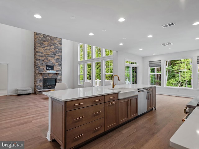 kitchen with dishwasher, wood-type flooring, sink, and a center island with sink