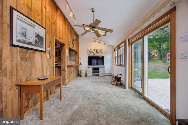 unfurnished living room with lofted ceiling, rail lighting, light carpet, wooden walls, and ceiling fan