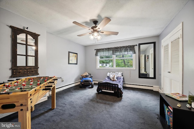 recreation room featuring a textured ceiling, ceiling fan, a baseboard heating unit, and dark colored carpet