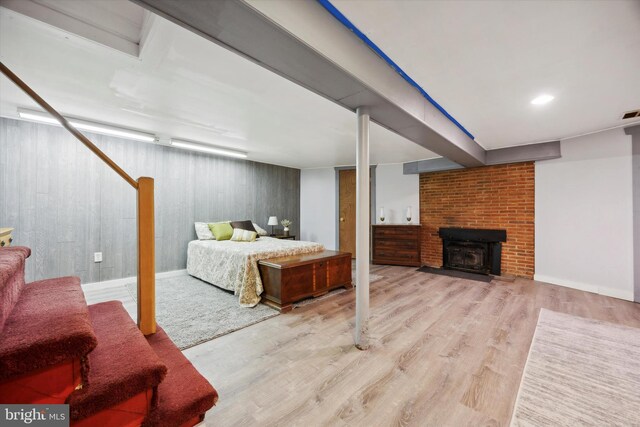 bedroom with a fireplace, wooden walls, light hardwood / wood-style flooring, and a wood stove