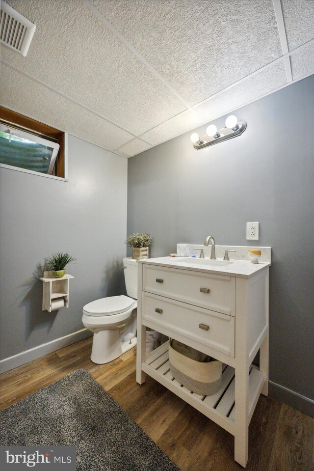 bathroom featuring vanity, a drop ceiling, hardwood / wood-style floors, and toilet