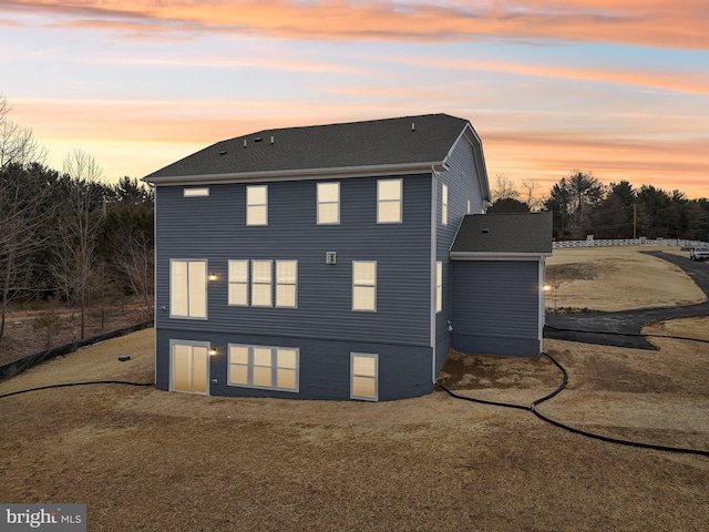 back house at dusk featuring a lawn