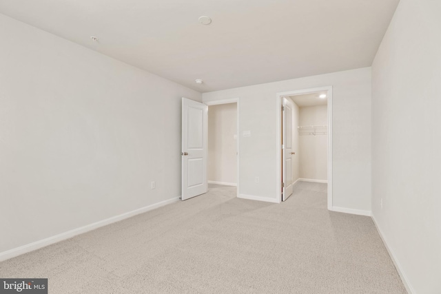 unfurnished bedroom featuring a walk in closet, light colored carpet, and a closet