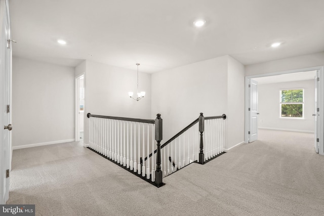 hallway featuring an inviting chandelier and light colored carpet