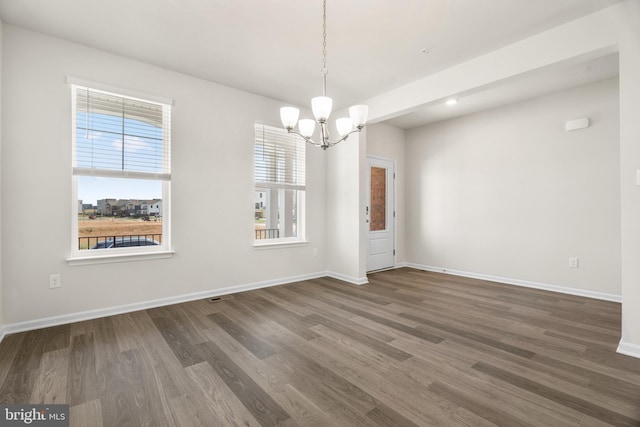 spare room with dark wood-type flooring and a chandelier