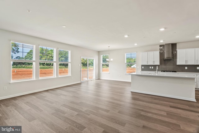 kitchen with tasteful backsplash, a center island with sink, white cabinets, hardwood / wood-style flooring, and wall chimney range hood