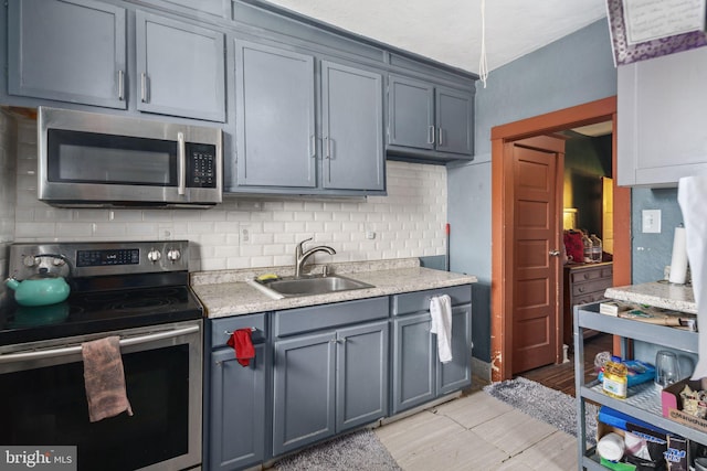 kitchen featuring tasteful backsplash, light tile patterned floors, gray cabinets, appliances with stainless steel finishes, and sink