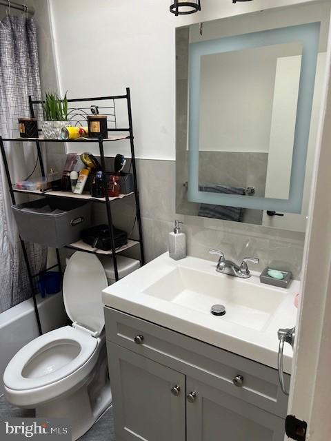 full bathroom featuring shower / bathtub combination with curtain, vanity, tile walls, and toilet