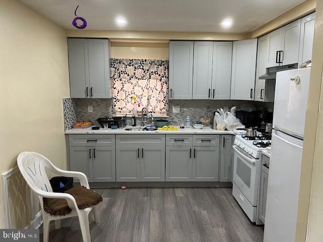 kitchen featuring gray cabinets, dark hardwood / wood-style flooring, white appliances, sink, and backsplash