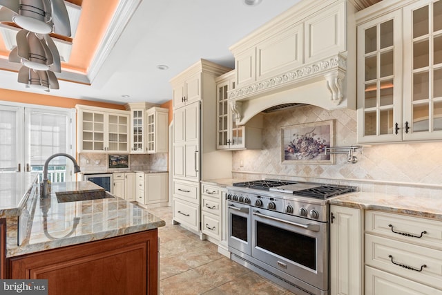 kitchen featuring range with two ovens, light stone countertops, cream cabinets, and sink