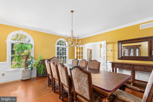 dining space featuring wood-type flooring, plenty of natural light, an inviting chandelier, and crown molding