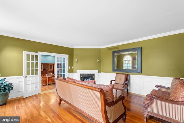 living room featuring a premium fireplace, wood-type flooring, ornamental molding, and french doors