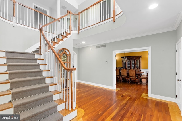 stairs with hardwood / wood-style flooring, a towering ceiling, and ornamental molding