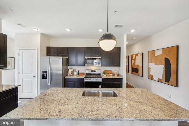 kitchen featuring pendant lighting, sink, appliances with stainless steel finishes, dark brown cabinets, and a center island with sink