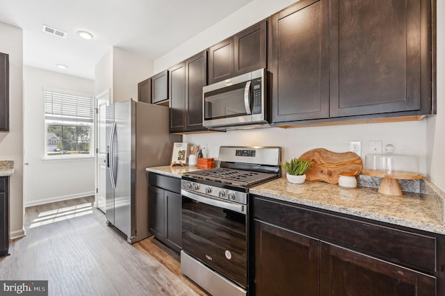 kitchen with light hardwood / wood-style flooring, light stone counters, dark brown cabinets, and stainless steel appliances