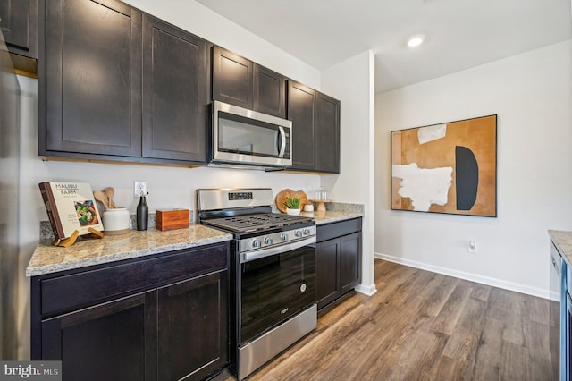 kitchen with light stone counters, hardwood / wood-style floors, dark brown cabinets, and stainless steel appliances