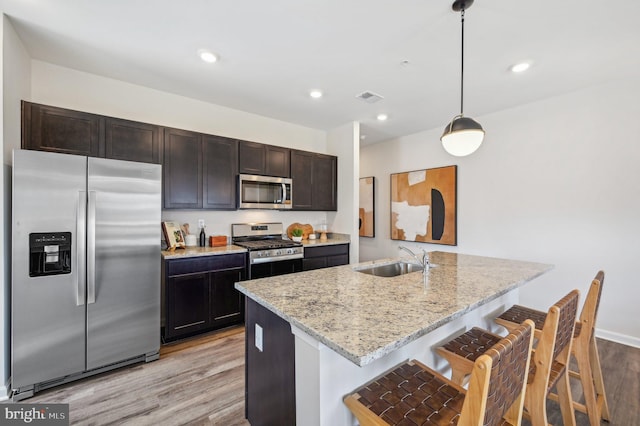 kitchen with pendant lighting, sink, a kitchen island with sink, stainless steel appliances, and light wood-type flooring