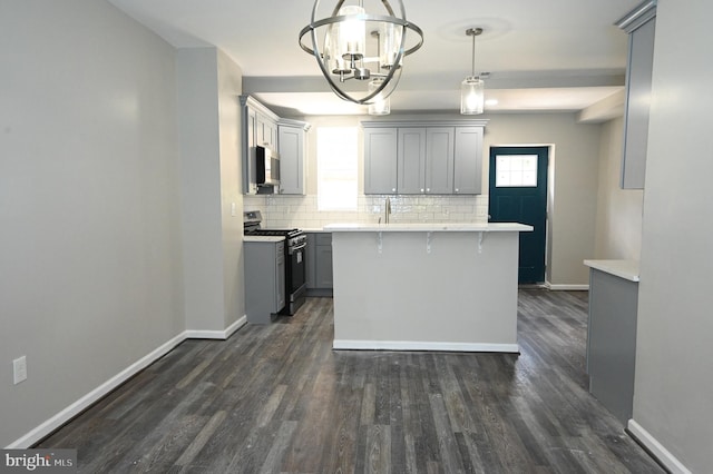 kitchen featuring gray cabinets, appliances with stainless steel finishes, a breakfast bar, decorative light fixtures, and backsplash