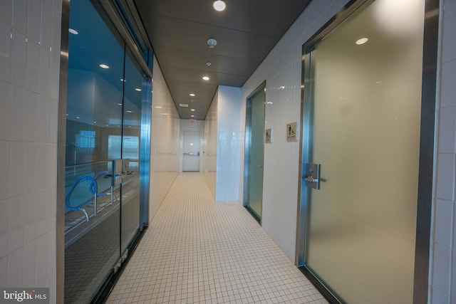 hallway featuring light tile patterned flooring and tile walls