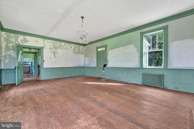 empty room with radiator heating unit, ornamental molding, an inviting chandelier, and hardwood / wood-style flooring