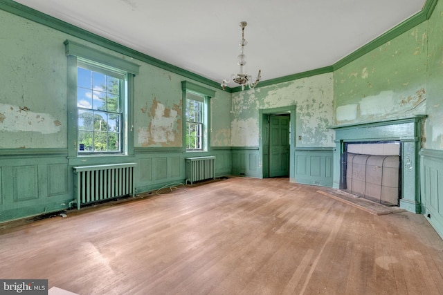 empty room featuring hardwood / wood-style flooring, an inviting chandelier, crown molding, and radiator