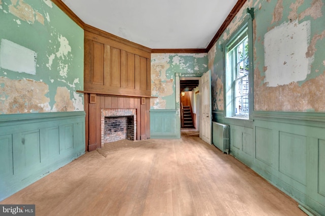 unfurnished living room featuring a fireplace, light hardwood / wood-style floors, ornamental molding, and radiator