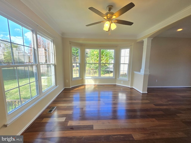 empty room featuring decorative columns, ornamental molding, dark hardwood / wood-style floors, and ceiling fan