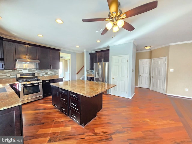 kitchen featuring a kitchen island, appliances with stainless steel finishes, tasteful backsplash, hardwood / wood-style flooring, and light stone counters