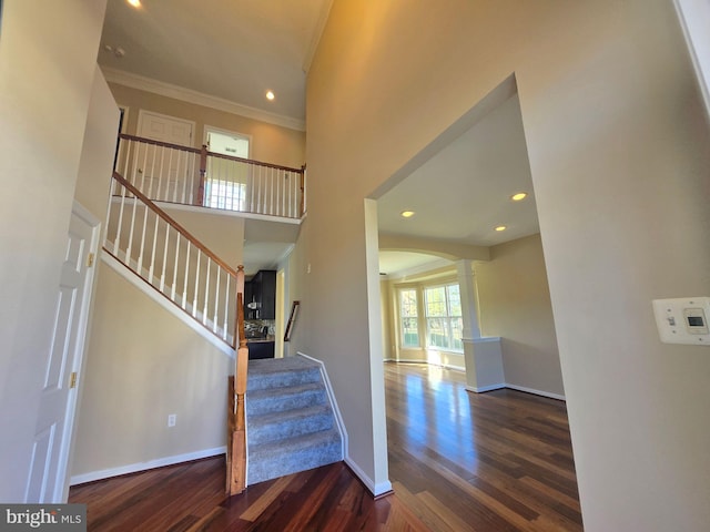 stairway with hardwood / wood-style flooring, a towering ceiling, crown molding, and decorative columns