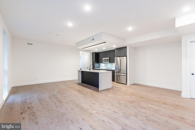 kitchen with light wood-type flooring, stainless steel appliances, a center island with sink, and sink