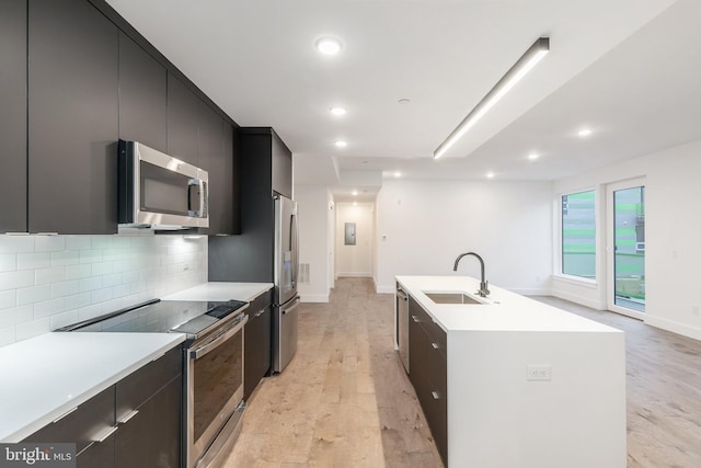 kitchen featuring light hardwood / wood-style flooring, tasteful backsplash, an island with sink, stainless steel appliances, and sink