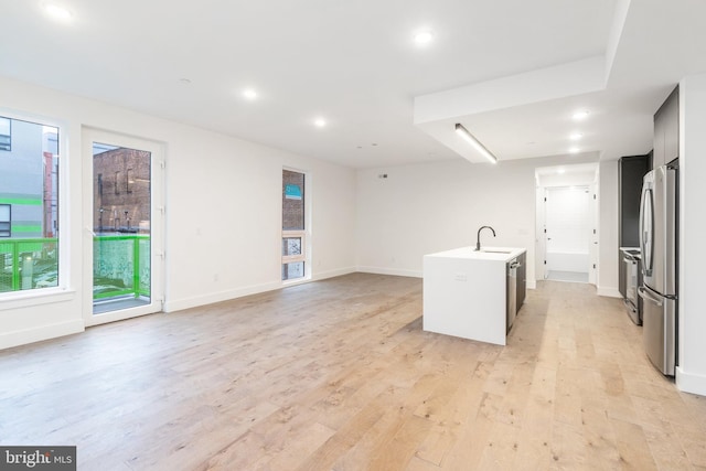 kitchen with stainless steel fridge, an island with sink, sink, and light hardwood / wood-style floors