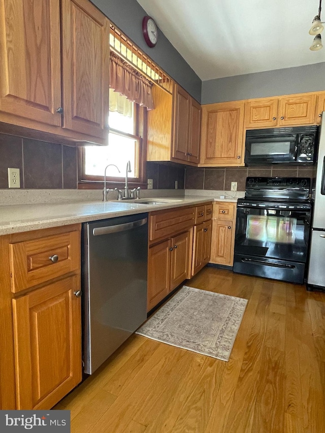 kitchen with light wood-type flooring, black appliances, backsplash, and sink