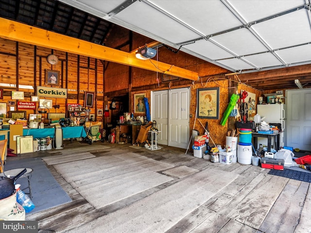 garage with a garage door opener, wooden walls, and freestanding refrigerator